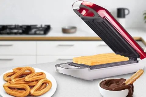Máquina para hacer churros abierta con churros dentro, plato de churros y tazón de chocolate.