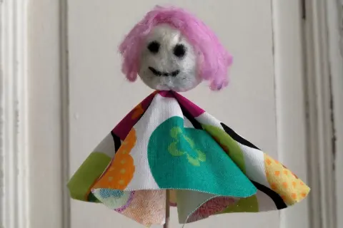 Eine selbstgemachte Puppe mit pinker Wolle als Haar und buntem Stoffkleid. Perfekt zum Filzen mit Kindern.