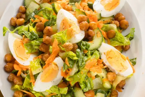 Ein bunter gemischter Salat mit knackigem Salat, Gurkenscheiben, geraspelten Karotten, Kichererbsen und gekochten Eiern.