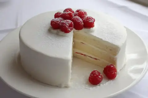 En vacker white lady tårta med fluffig grädde och färska hallon. En bit är bortskuren och visar de läckra lagren.