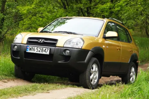 Złoty Hyundai Tucson 2007 na leśnej drodze, gotowy na przygodę.
