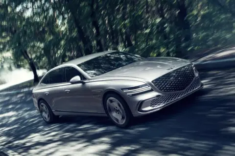 Silver Genesis G80 Sverige glider genom en skogsväg, skuggor dansar över bilen.