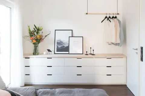 Ideas para decorar cómoda dormitorio matrimonio: ramo de flores, cuadros, velas y ropa colgada.