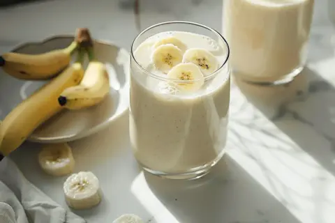 Pyszny koktajl bananowy, ozdobiony plasterkami banana, obok świeżych owoców na talerzyku. Idealny na orzeźwiający początek dnia.