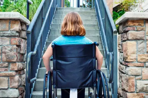Ragazza in carrozzina affronta una scalinata, un aiuto per l'accessibilità come previsto dalla legge 104.
