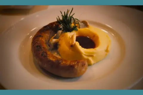 Une saucisse grillée, courbée sur une purée onctueuse, garnie de romarin et de sauce. Un plat réconfortant de saucisse purée.
