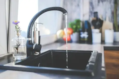Ein Wasserhahn tropft in eine Spüle. Ein kleiner Strauß Blumen steht daneben. Dies könnte ein Hinweis auf den Kaltwasserverbrauch pro Person sein.