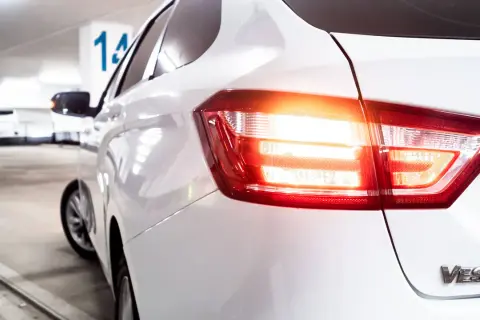 Vue arrière d'une voiture blanche dans un parking. Les feux de recul obligatoires sont allumés, signalant un départ imminent.