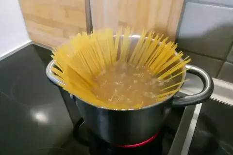 Długi makaron spaghetti gotuje się w garnku z wrzącą wodą. Czas gotowania jest kluczowy, by był idealnie al dente.