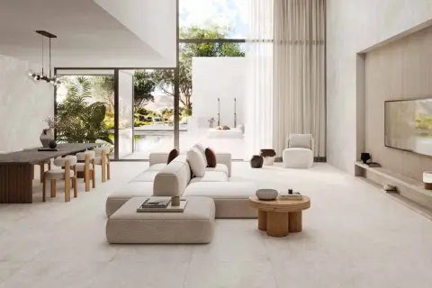 Salon lumineux avec canapé blanc, table à manger en bois et sol en **couleur béton ciré**. Vue sur une piscine et un jardin luxuriant.