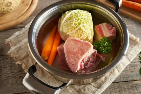 Une marmite de **potée au chou** avec des os de bœuf, des carottes, du chou et du persil, prête à mijoter.