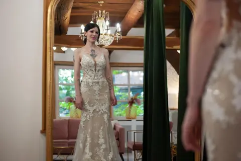 Braut steht vor Spiegel in einem figurbetonten Brautkleid mit Tüll und Spitze.
