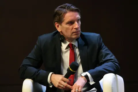 Tomasz Lis w garniturze i czerwonym krawacie, z mikrofonem w dłoni. Mówi o swojej chorobie.