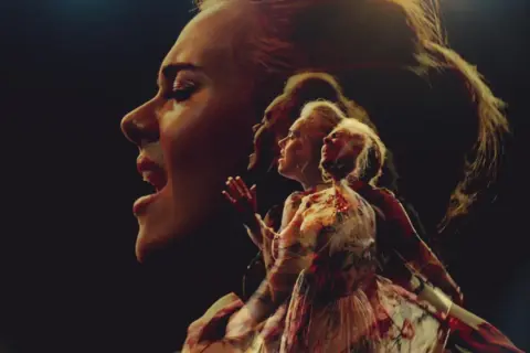 Adele śpiewa "Send My Love" w wielokrotnej ekspozycji, jej twarz i postać w sukni rozmywają się w mroku.