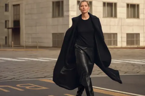 Elegancka kobieta w czarnej, skórzanej spódnicy i płaszczu. Idealna stylizacja, która pokazuje, jaka bluzka do skórzanej spódnicy pasuje najlepiej.