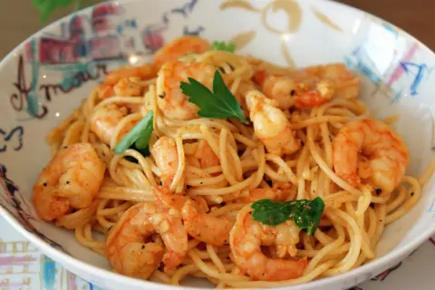 Un plat de pâtes aux crevettes, garni de persil frais, servi dans un bol décoré. Un délice pour les yeux et les papilles.