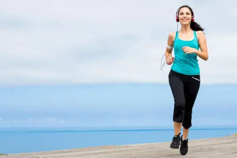 Mujer sonriente corriendo junto al mar, disfrutando de ejercicios para trabajar la autoestima y sentirse bien.