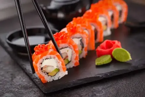 Chopsticks podnoszą kawałek sushi z łososiem i ikrą. Czy sushi jest lekkostrawne? Zależy od składników, ale to danie wygląda apetycznie.