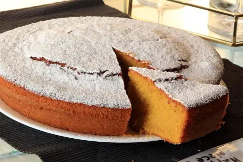 Una soffice torta carote e mandorle, cosparsa di zucchero a velo, con una fetta tagliata che ne rivela l'interno dorato.