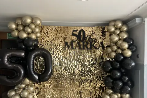 Złote i czarne balony otaczają błyszczące tło z napisem "50 lat Marka".