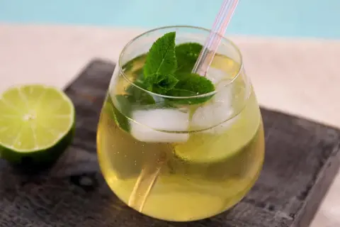 Erfrischender alkoholfreier Hugo mit Minze, Limette und Eiswürfeln, serviert in einem Glas mit Strohhalm.