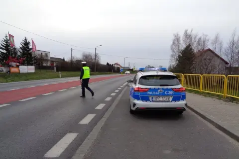 Policjant w kamizelce odblaskowej kieruje ruchem obok radiowozu. Może to być kontrola drogowa lub reakcja na wykroczenie 97 kw.