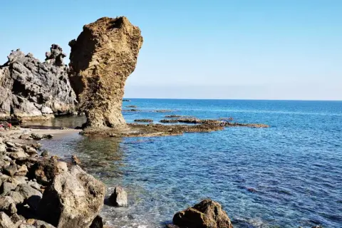 Rocas erosionadas y mar azul en la playa El Sombrerico. Una formación rocosa alta se alza como un guardián.