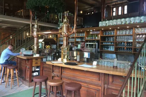 Gemütliche Atmosphäre im Brauhaus Spandau. Ein Mann sitzt am Tresen, hinter ihm Regale voller Gläser und Bierfässer.