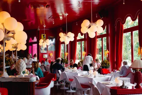 Ein lebhaftes **Cafe Berlin Mitte** mit roten Wänden, auffälligen Kugelleuchten und Gästen, die an weiß gedeckten Tischen sitzen.
