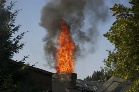 Flammen schlagen aus einem Schornstein, dunkler Rauch steigt auf. Ob man Europaletten verbrennen darf, ist fraglich.