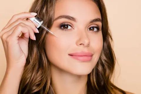Kobieta aplikuje serum z pipetki na policzek. Dowiedz się, jak stosować retinol dla pięknej cery.