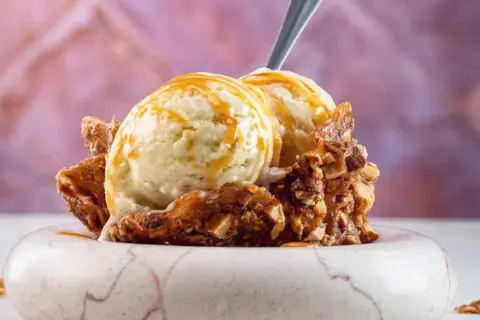 Zwei Kugeln cremiges Eis mit Honig statt Zucker, garniert mit karamellisierten Nüssen und einem Löffel.