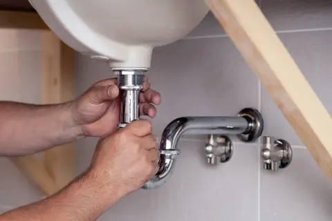 Hände schrauben am Siphon unter dem Waschbecken. Ein Handwerker reinigt den Siphon, um Verstopfungen zu beseitigen.
