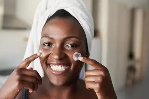 Lächelnde Frau mit Handtuch auf dem Kopf trägt Creme auf. Frage: Retinol wie oft?