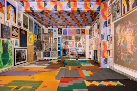 Vibrant art fills a room, from the ceiling posters to the floor rugs, showcasing the diverse creativity of Mexico City Art Week.