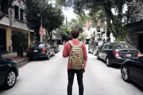 Ein junger Mann mit Rucksack steht auf einer Straße in Mittelamerika, bereit für sein nächstes Abenteuer beim Backpacking.