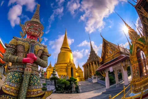 Imponerande tempel i Bangkok med en stor, färgglad jättefigur framför gyllene pagoder under en blå himmel med moln.