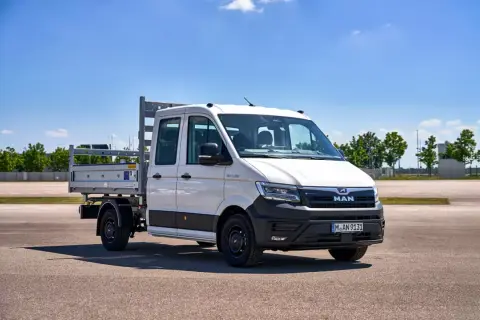 Camionnette MAN blanche avec plateau, prête pour le **c tuning** et le travail. Ciel bleu et verdure en arrière-plan.