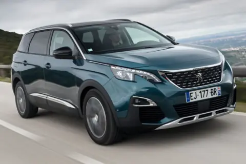 Peugeot 5008 wady i zalety: zielony SUV jedzie po krętej drodze z widokiem na góry.