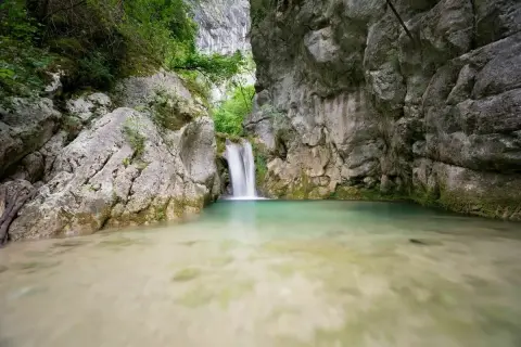 Cascade d'eau tombant dans un bassin turquoise au cœur de la gorge du Nan, entourée de falaises rocheuses et de végétation luxuriante.