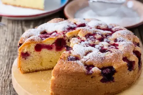 Puszyste ciasto z porzeczkami, posypane cukrem pudrem, wygląda apetycznie. Jeden kawałek już zniknął!