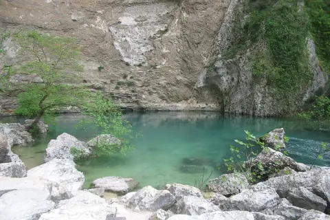Le gouffre de la Fontaine de Vaucluse, une eau turquoise limpide émergeant d'une falaise rocheuse, entourée de végétation luxuriante et de rochers.