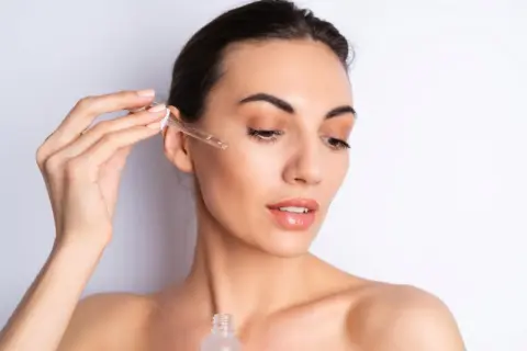 Una mujer aplica serum en su rostro con un gotero. Así se aplica el serum para una piel radiante.