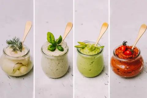 Vier Gläser mit selbstgemachtem Brotaufstrich: cremig-hell mit Dill, grün mit Basilikum, Avocado-grün und rot mit Tomaten.