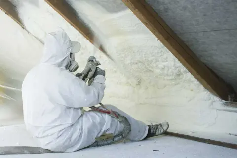 Operaio in tuta protettiva applica schiuma espansa per un efficace isolamento termico del sottotetto.