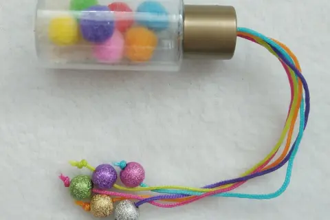 Buntes Rassel-Spielzeug zum selber machen 1 Jahr: Pompons in Fläschchen, bunte Schnüre mit Glitzerkugeln.
