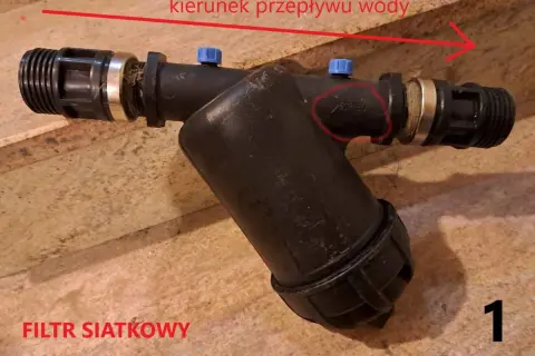 Filtr siatkowy w pionie, gotowy do montażu. Strzałka wskazuje kierunek przepływu wody.