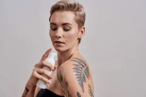 Kobieta z kolorowym tatuażem na ramieniu aplikuje piankę. Dowiedz się, czym myc tatuaz, by zachować jego piękno.