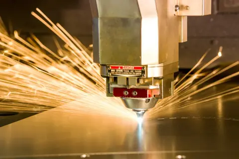 Precyzyjne cięcie metalu przez laser przemysłowy, iskry rozchodzą się na boki.