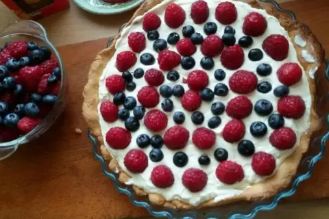 Pyszna tarta na słodko z malinami i borówkami, udekorowana kremem. Idealna na letnie popołudnie.